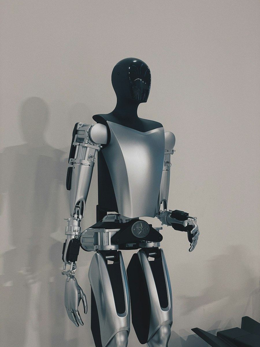 Full-body grey humanoid robot standing against a plain wall